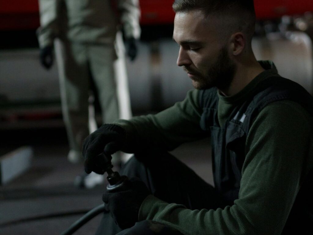 Two mechanics working on a vehicle engine inside a garage at night.